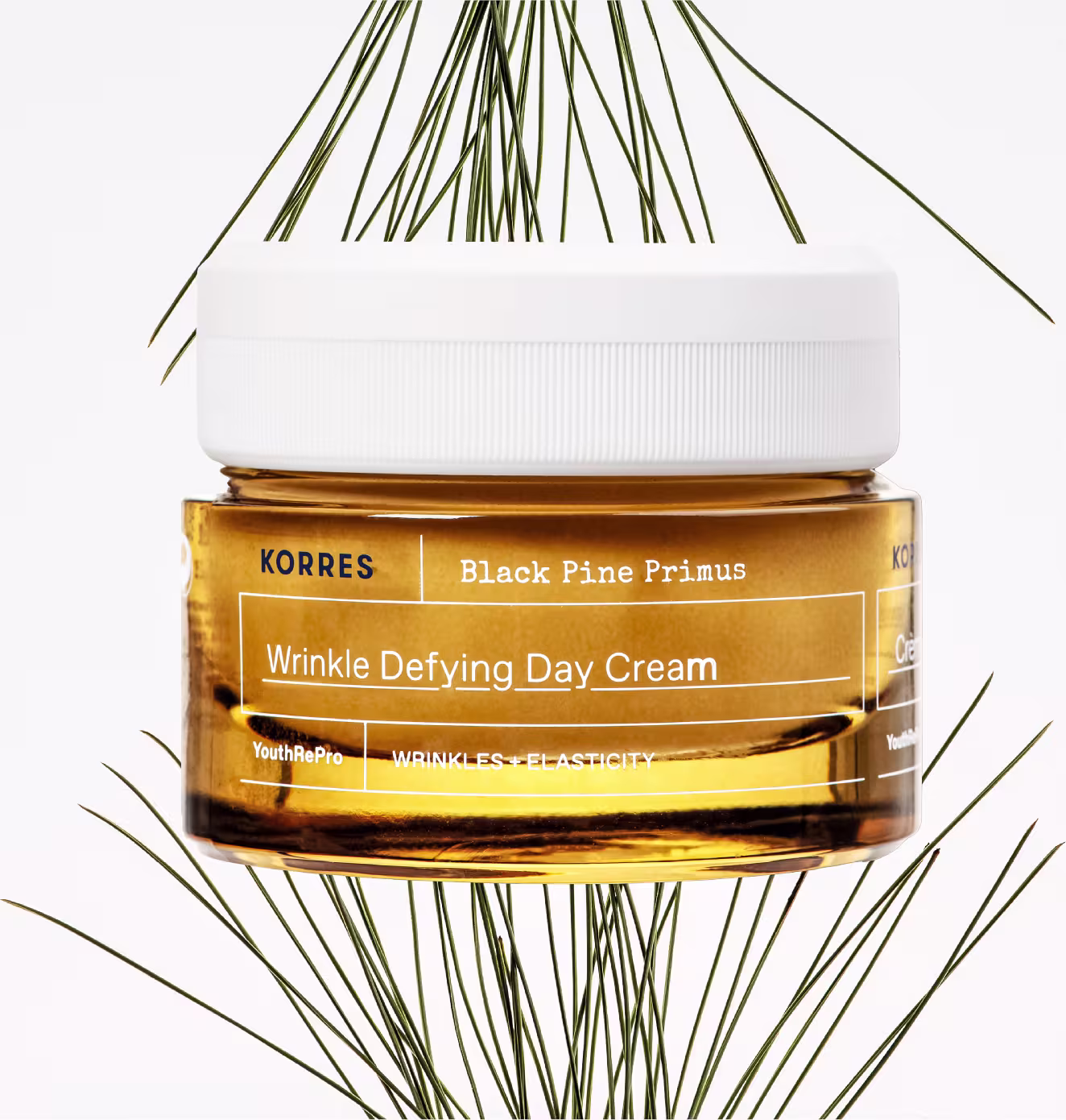 Frasco de creme antirrugas da marca Korres, com rótulo amarelo destacando o nome "Black Pine Primus" e a descrição "Wrinkle Defying Day Cream". O produto está cercado por galhos de pinheiro verde-escuro.