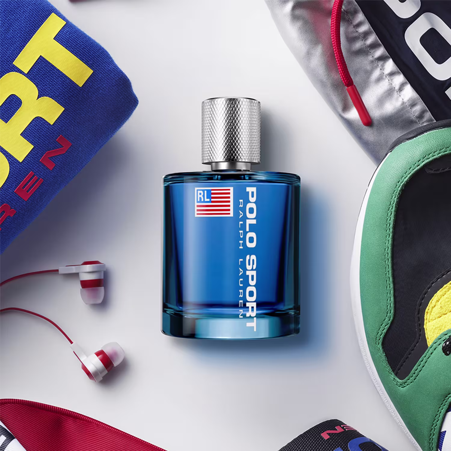 Frasco de item de perfumaria azul com rótulo vermelho, branco e azul contendo a bandeira dos Estados Unidos e o texto "POLO SPORT" em letras brancas. O frasco possui um design texturizado e um bico pulverizador metálico.