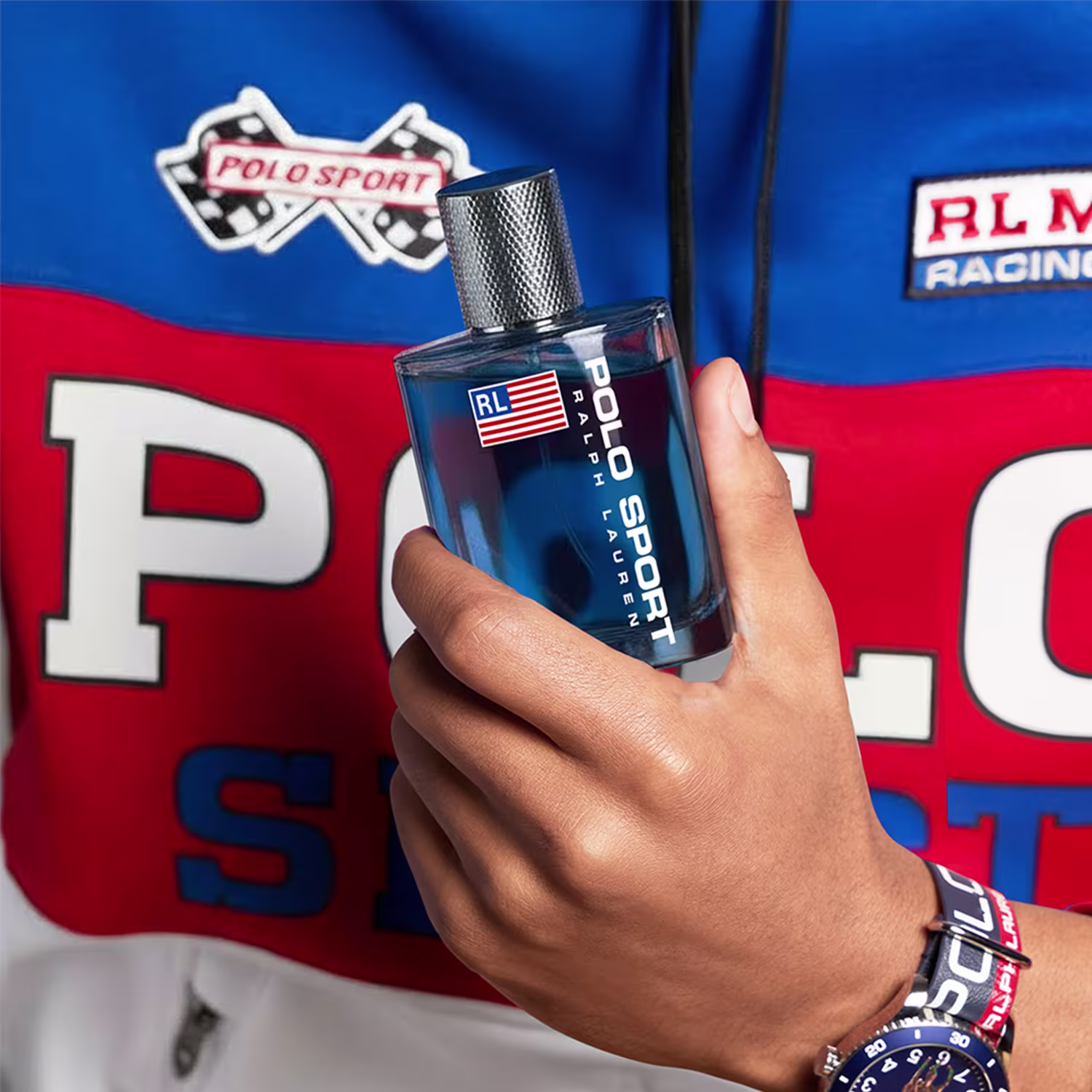 Frasco de item de perfumaria azul com rótulo vermelho, branco e azul contendo a bandeira dos Estados Unidos e o texto "POLO SPORT" em letras brancas. O frasco possui um design texturizado e um bico pulverizador metálico.