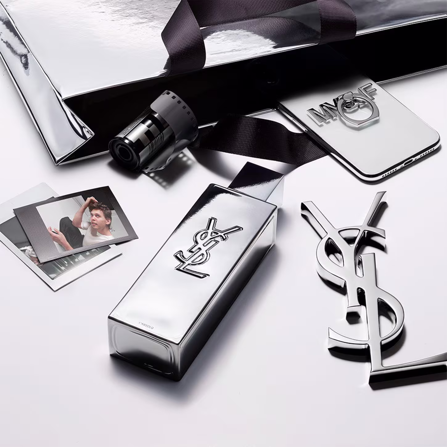 Frasco de perfume de design minimalista prateado, com o logotipo da marca Yves Saint Laurent em destaque. A embalagem possui uma forma geométrica simples e elegante, com uma tampa destacada no topo.