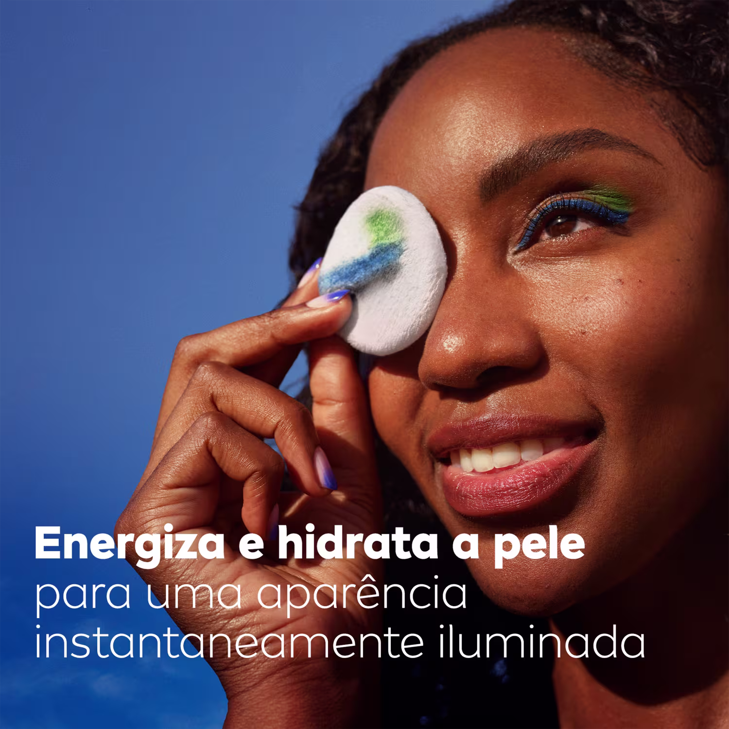 Uma mulher de pele escura aplica um produto cosmético branco em seu rosto, com texto "Energiza e hidrata a pele para uma aparência instantaneamente iluminada" visível na imagem.