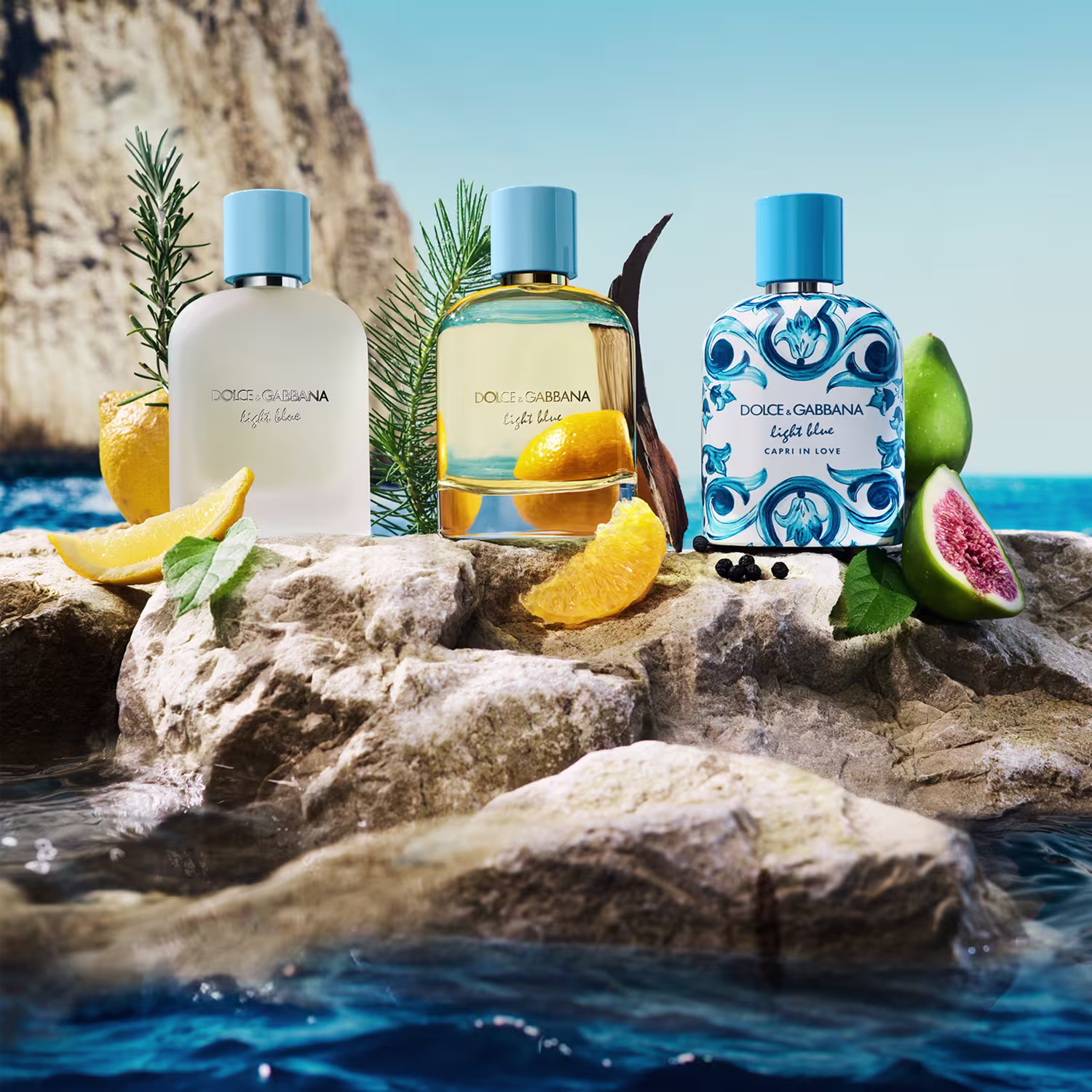 Perfume Dolce & Gabbana Light Blue em primeiro plano, com ramos de pinheiro, fatias de limão e pedras em um cenário de praia com mar azul e céu claro ao fundo.