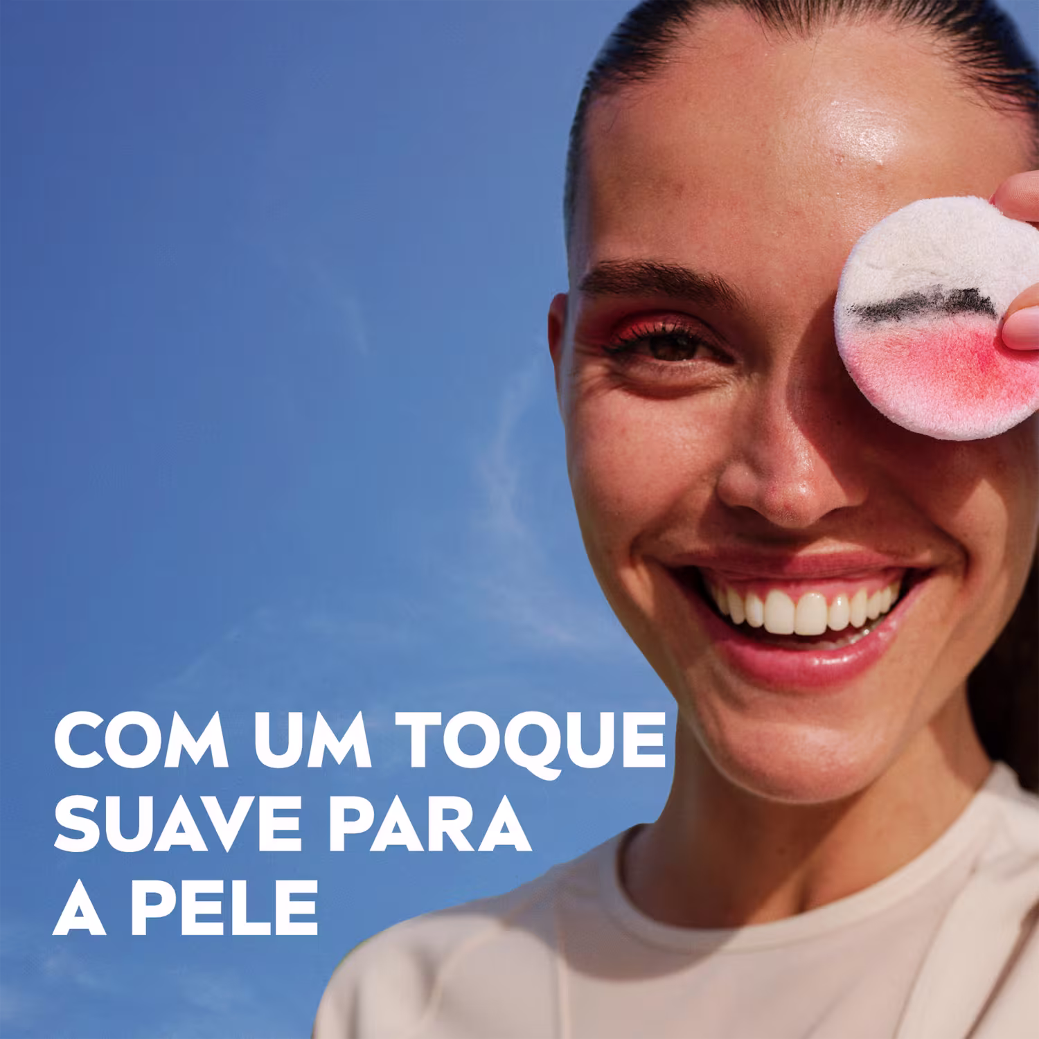 Uma mulher sorridente segura um item de perfumaria rosa com texto "Com um toque suave para a pele" visível.