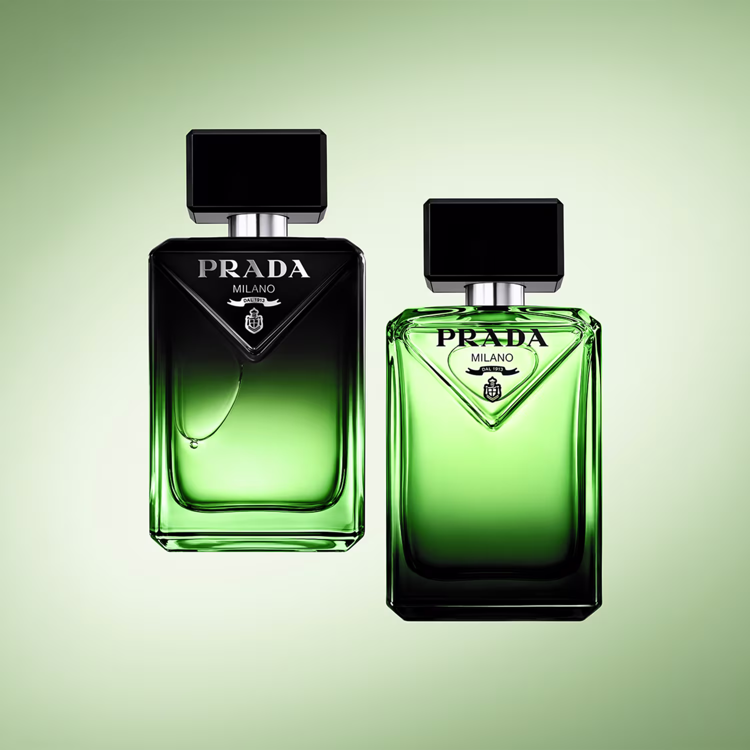 Dois frascos de perfume Prada Milano em tons de verde, com embalagens pretas e detalhes em prata. O frasco maior possui um design triangular, enquanto o menor tem um formato mais tradicional.
