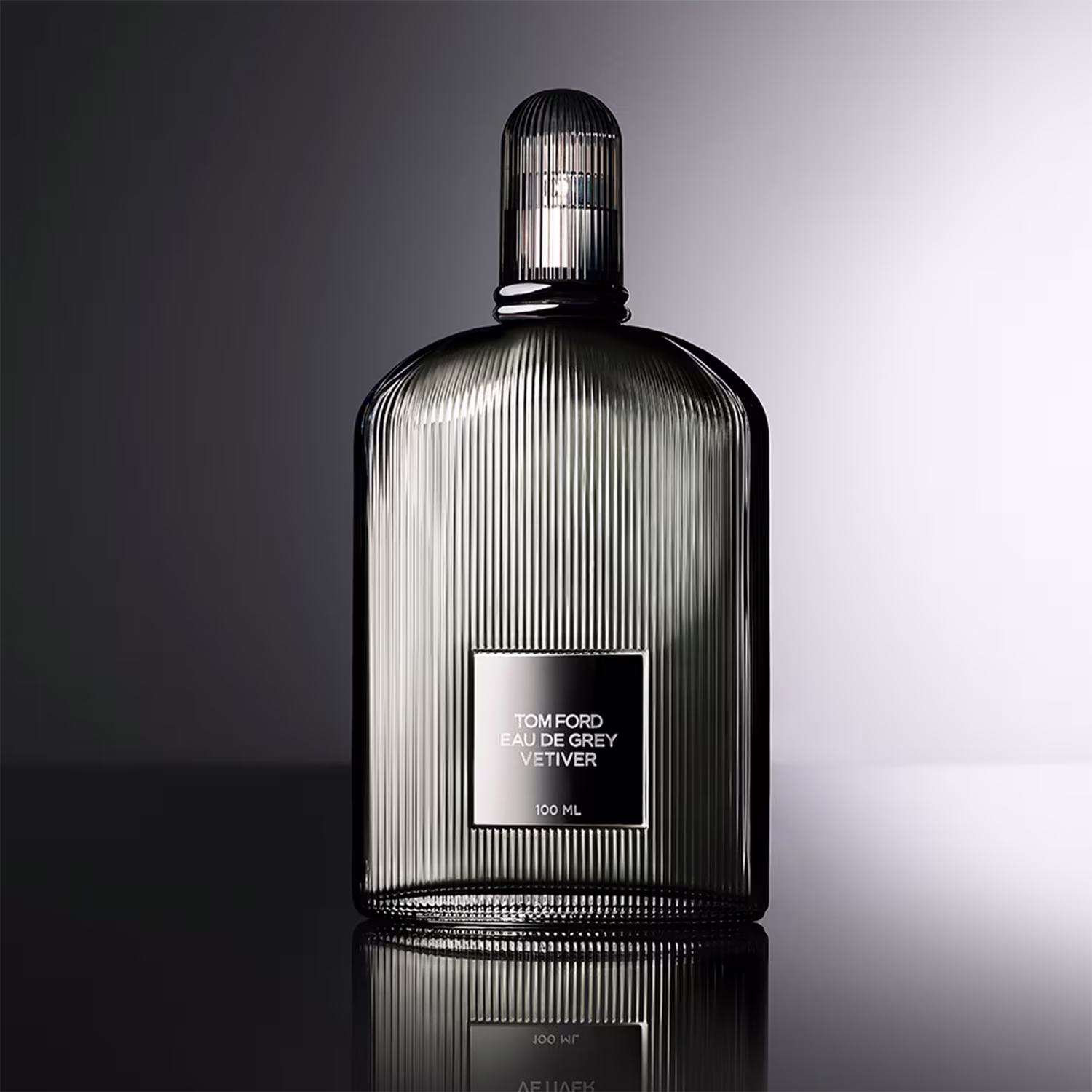 Frasco de perfume Tom Ford Eau de Grey Vetiver, com design de vidro estriado e tampa prateada. Rótulo branco com o nome da fragrância em letras pretas. Embalagem elegante e minimalista, com volume de 100 ml.