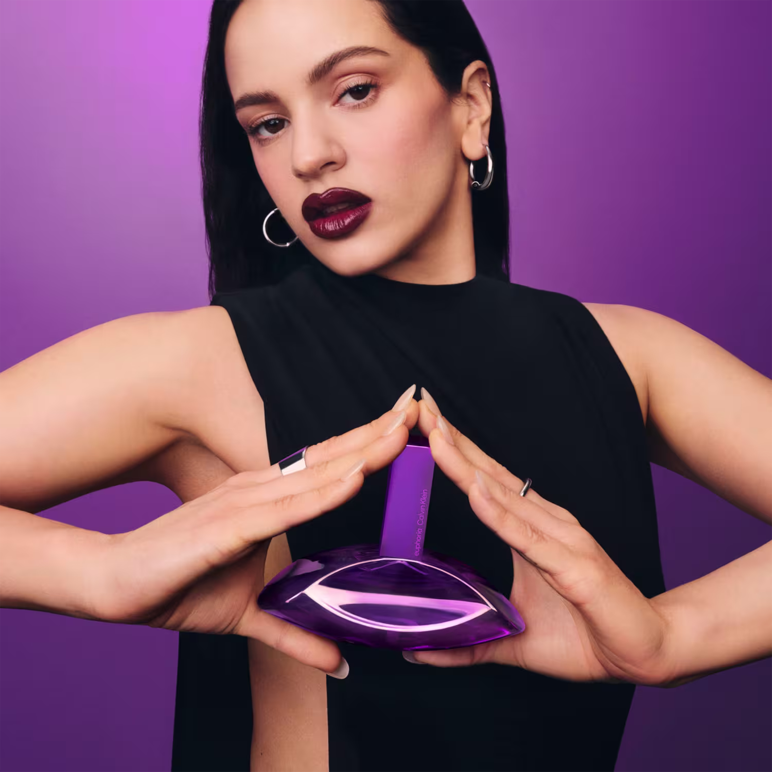 Frasco de item de perfumaria de cor violeta brilhante, com formato ovalado e tampa retangular. Rótulo com o texto "euphoria Calvin Klein" em letras brancas.