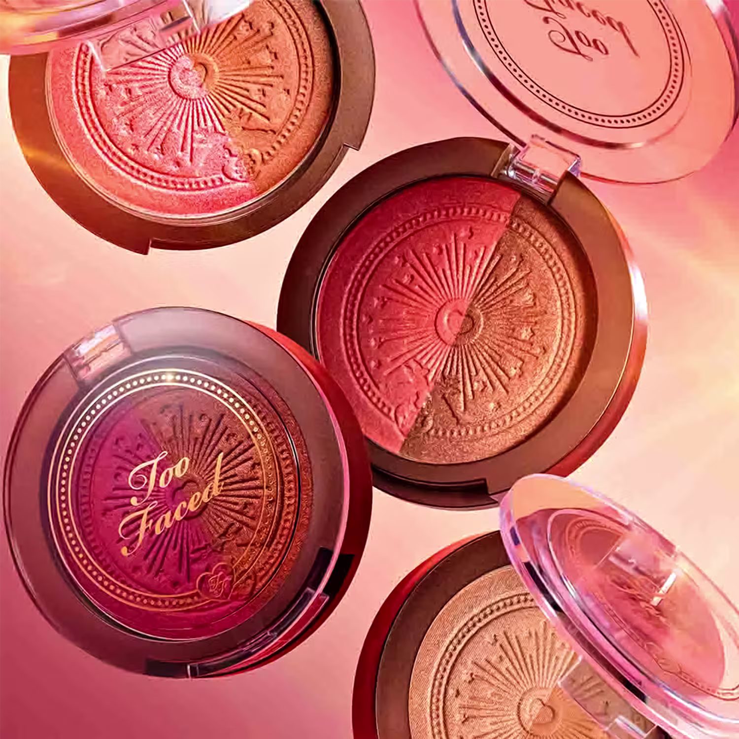 Imagem de produtos de maquiagem da marca Too Faced, com compactos de blush e pó em tons quentes de laranja e rosa, em um ambiente com iluminação suave e tons terrosos.