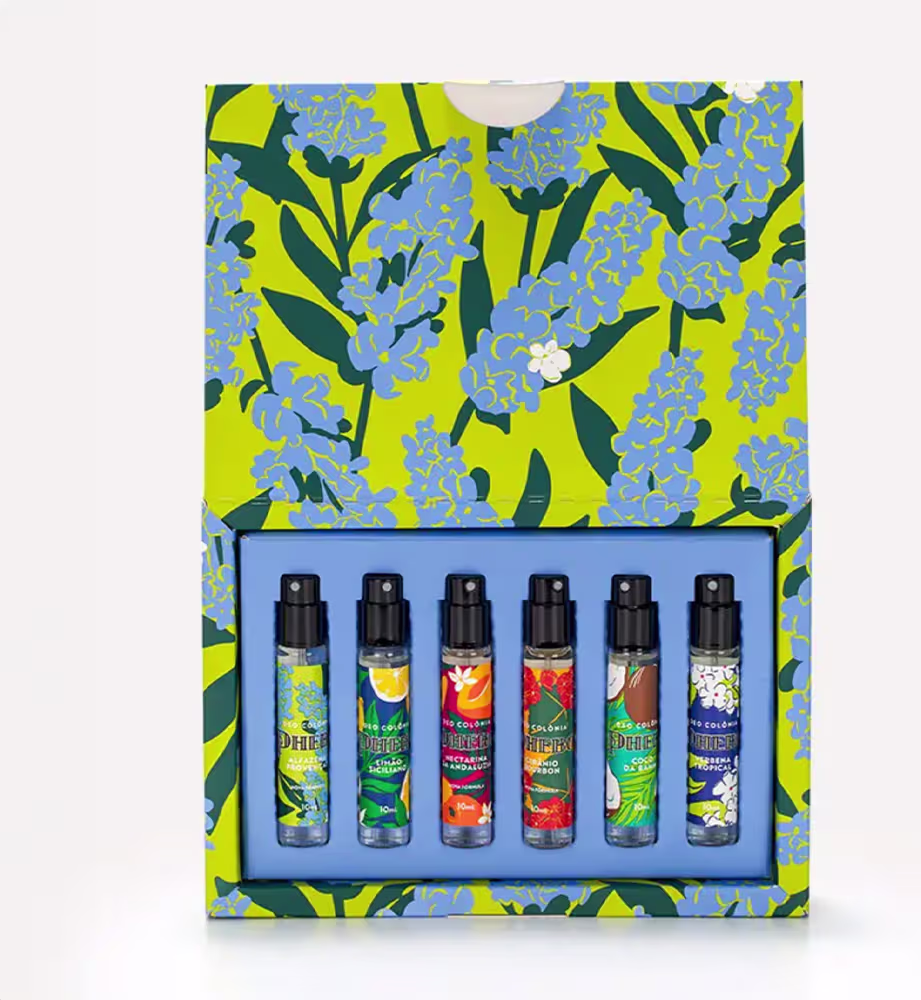 Caixa amarela com flores azuis e verdes, contendo diversos frascos de itens de perfumaria da marca Phebo em diferentes cores e formatos.