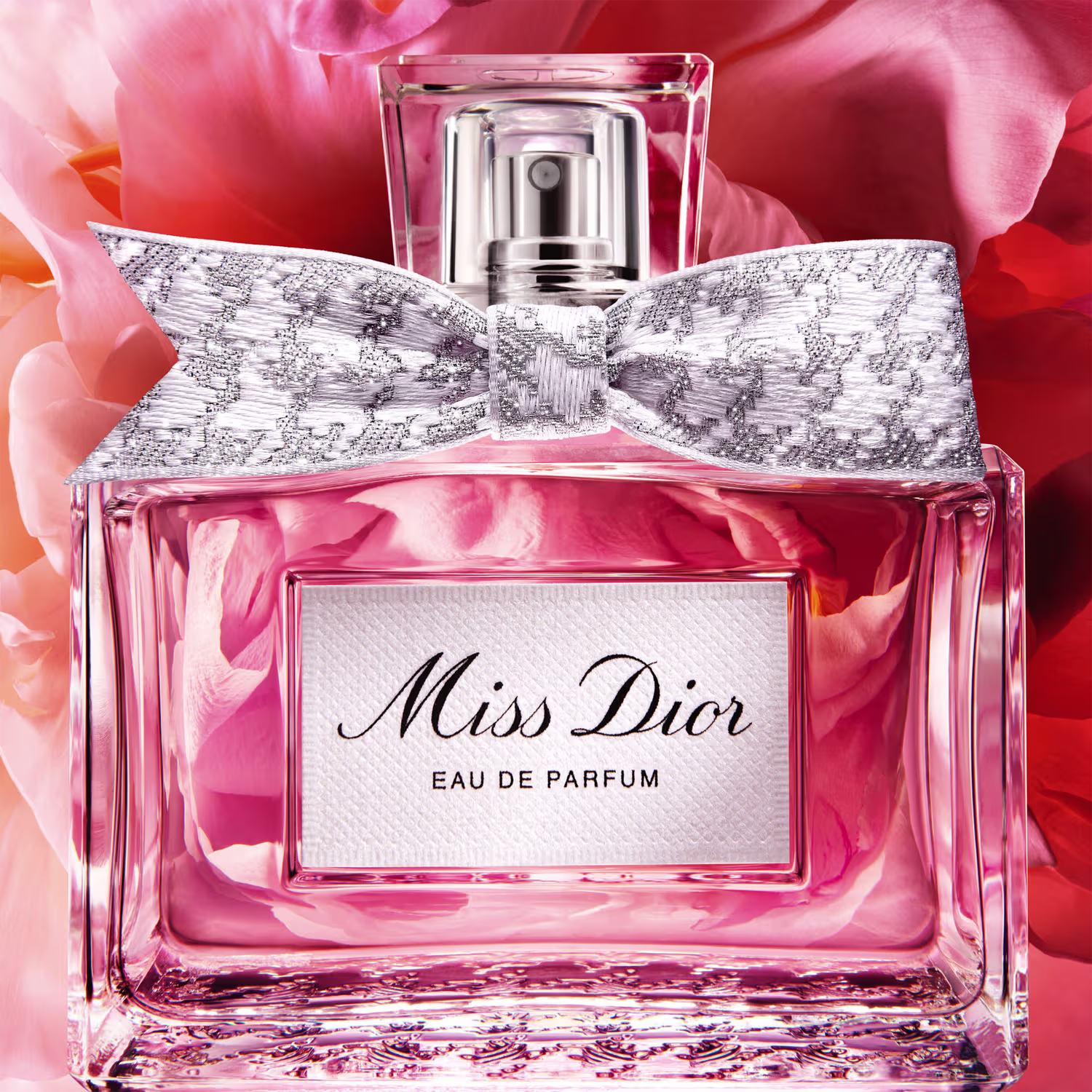 Frasco de perfume Miss Dior em formato retangular com tampa prateada. Embalagem com detalhes em renda branca e rosa claro, com texto "Miss Dior Eau de Parfum" em destaque.