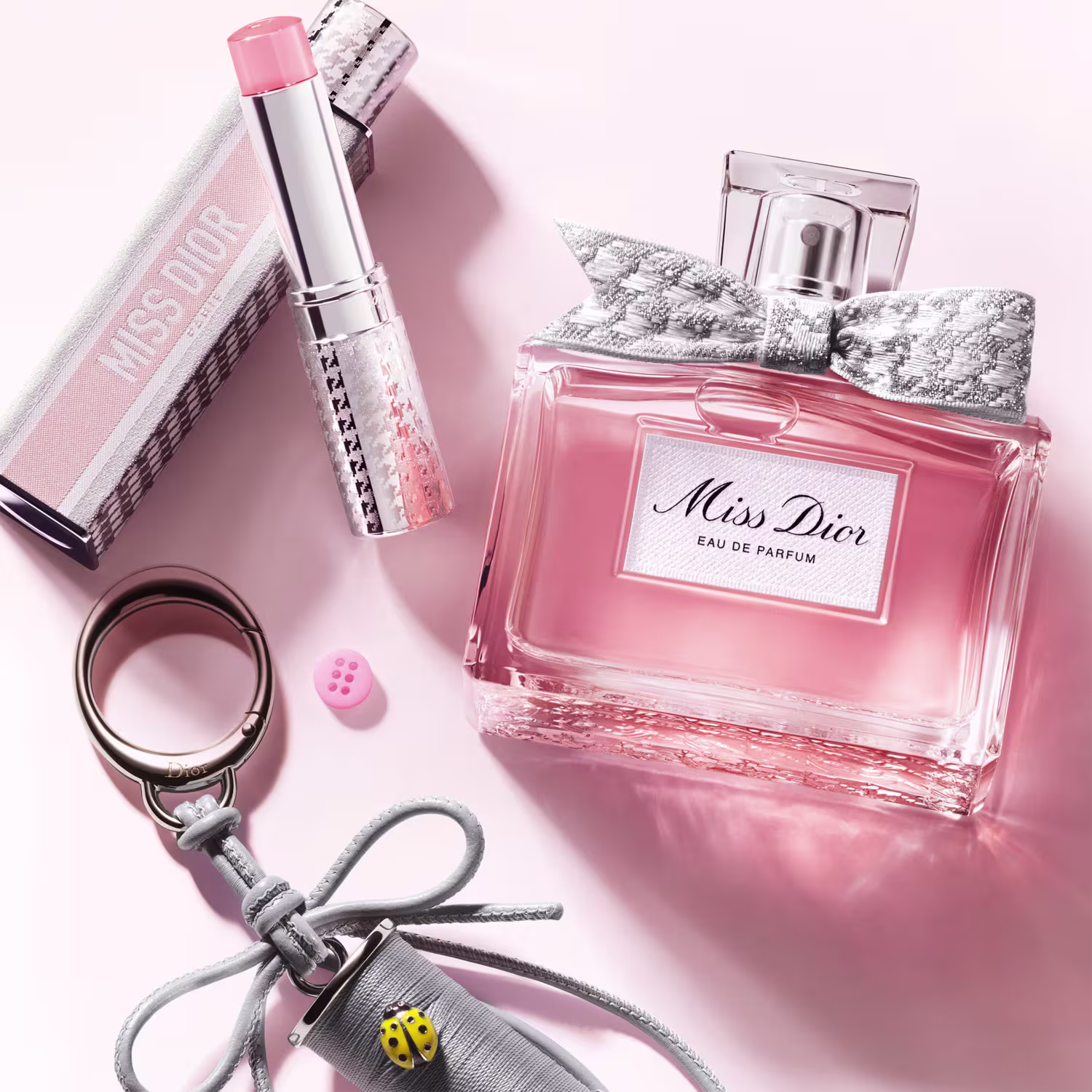 Perfume Miss Dior, batom e acessórios em tons de rosa e cinza, sugerindo um contexto elegante e sofisticado.
