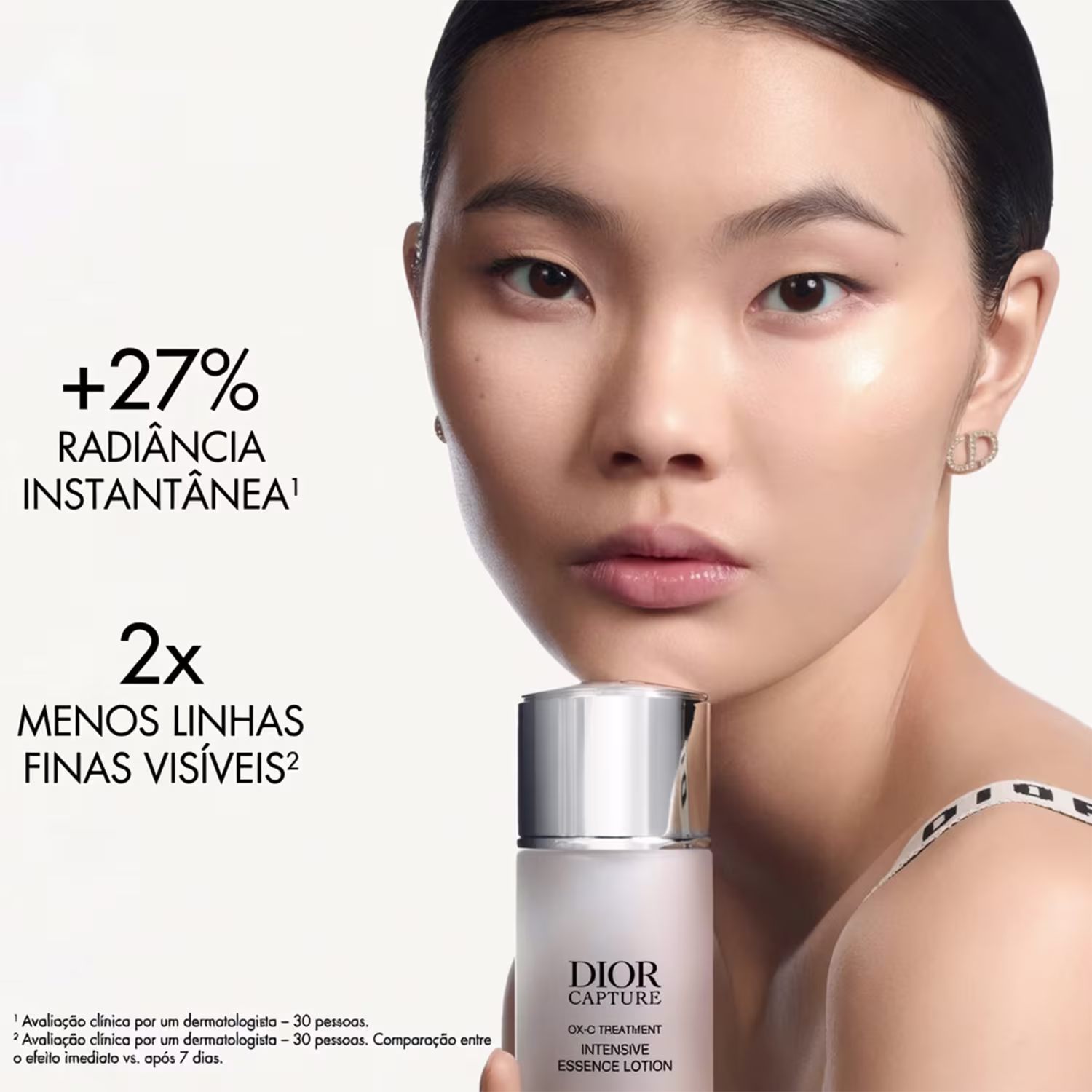 Uma mulher asiática com cabelos escuros e expressão séria segurando o produto da marca Dior, com texto "Dior Capture OX-C Treatment Intensive Essence Lotion" e "+27% radiância instantânea" visível.