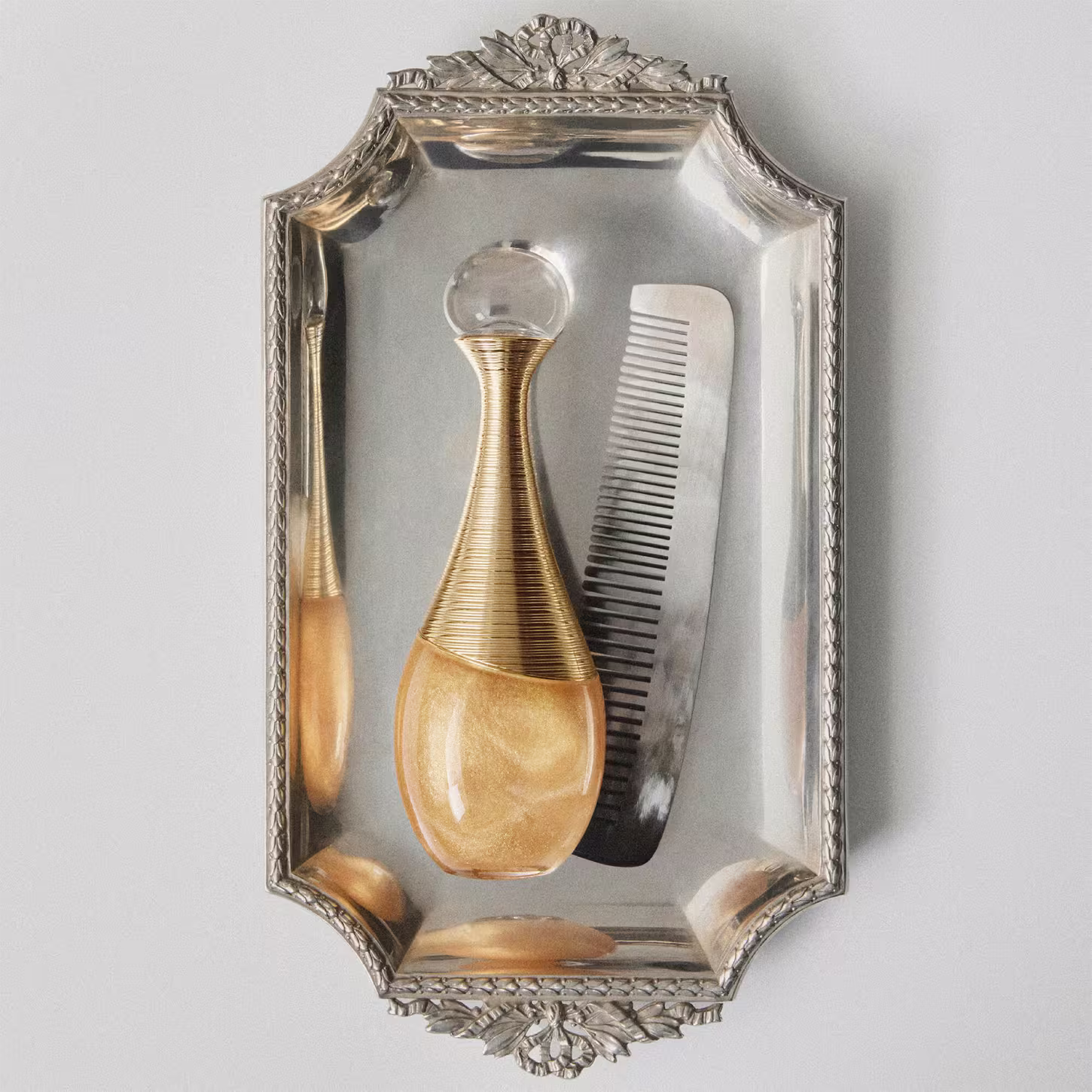 Frasco de perfume para cabelo Dior em formato de gota, com corpo dourado e detalhes em fios dourados entrelaçados, tampa transparente redonda. Embalagem elegante e sofisticada.