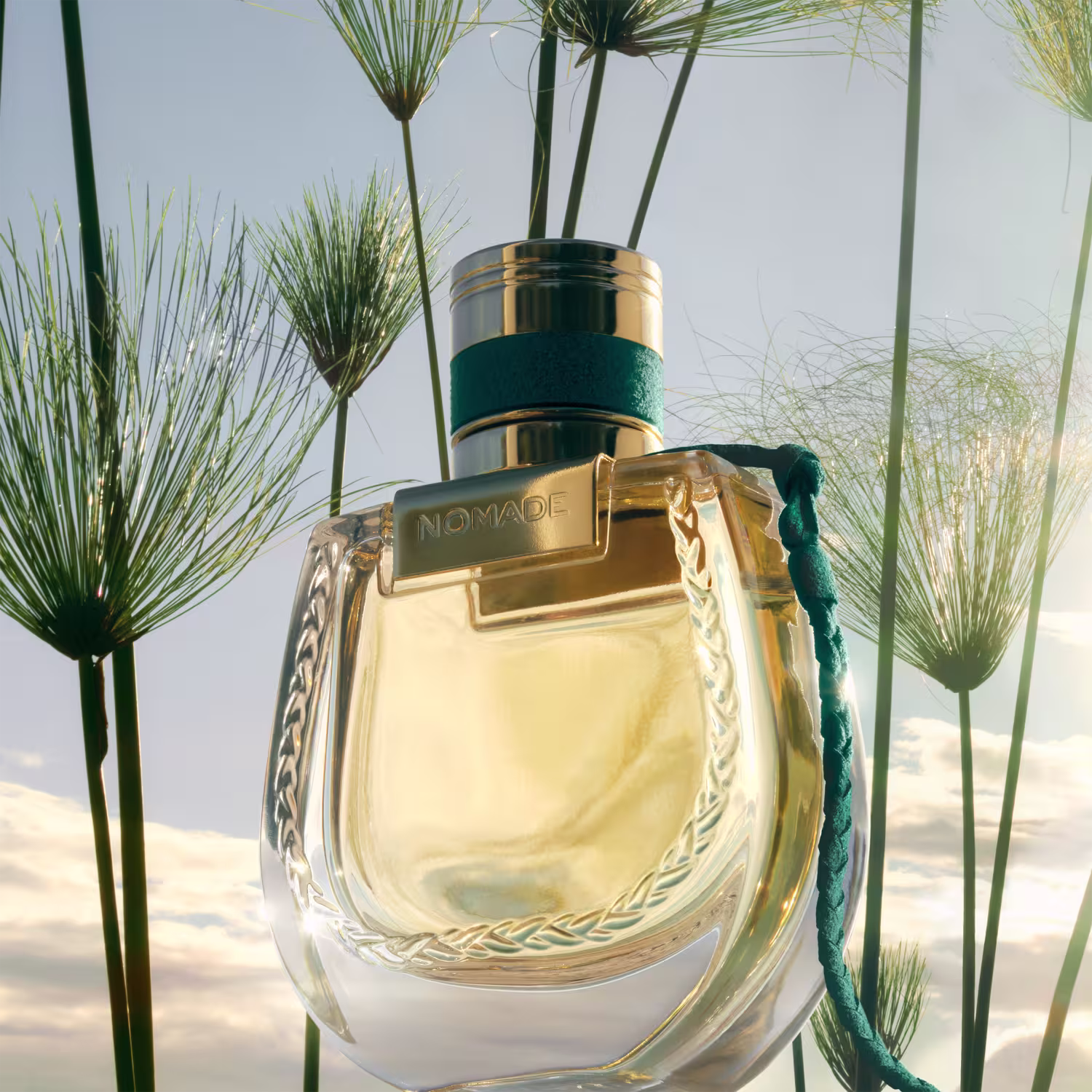Ambiente natural com vegetação exuberante, onde um frasco de perfume Chloé Nomade Jardin d'Egypte se destaca com seu design elegante e detalhes em dourado, sugerindo um jardim egípcio