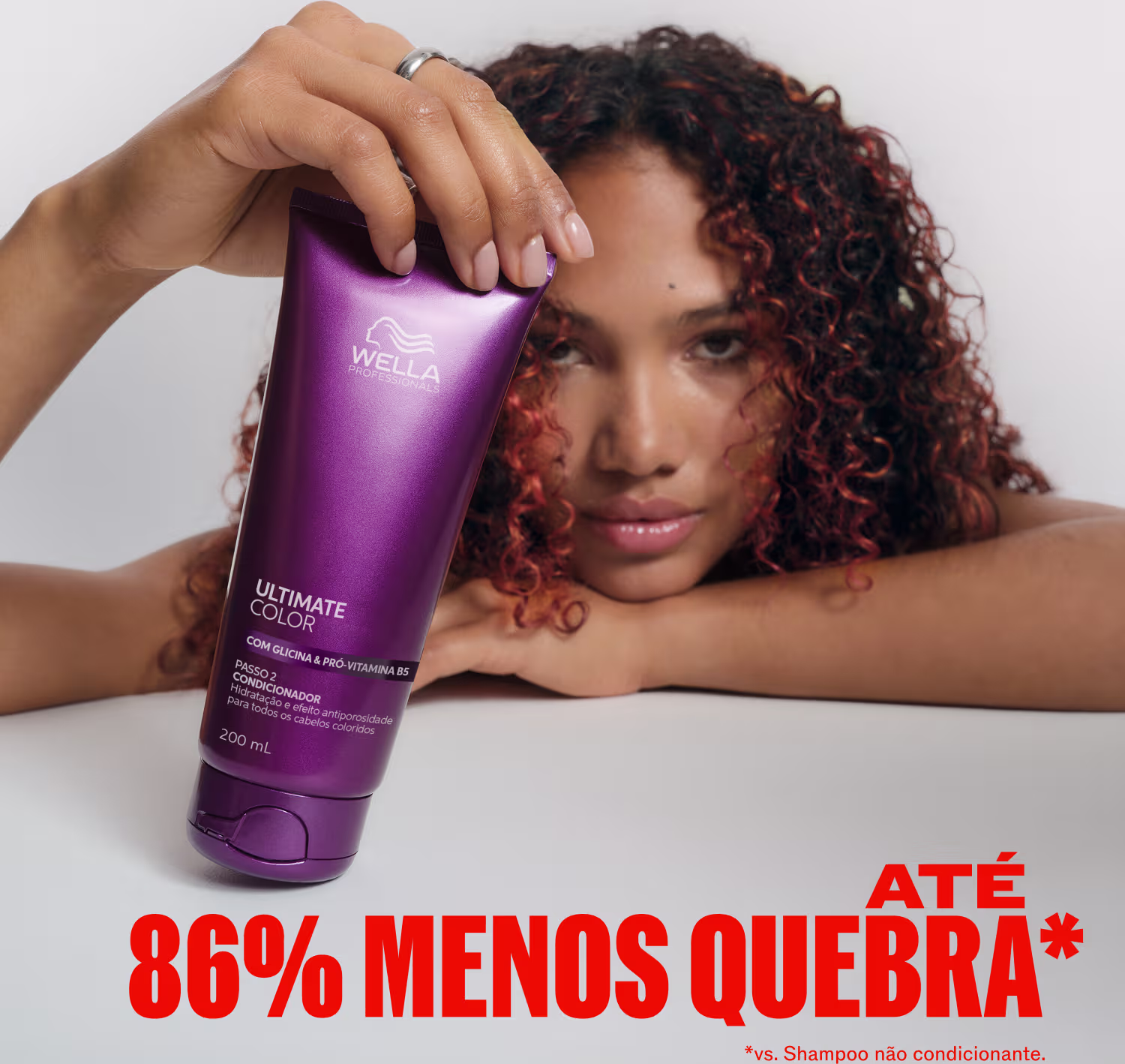 A modelo com cabelos cacheados segura um frasco roxo da linha Ultimate Color da Wella Professionals, destacando o benefício de 86% menos quebra em comparação ao uso de shampoo não condicionante.