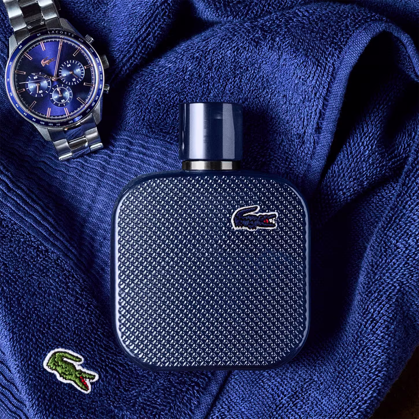 Frasco de perfume Lacoste de cor azul escuro, com textura de couro e logotipo da marca em destaque. Embalagem elegante e minimalista, com tampa preta.