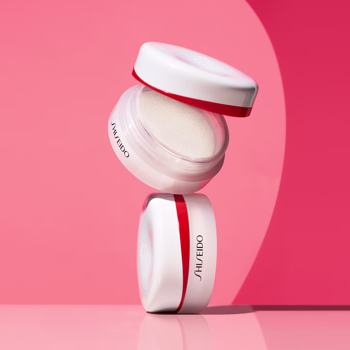 Pote branco e vermelho de item de perfumaria da marca Shiseido, com tampa e rótulo em destaque, sobre fundo rosa.