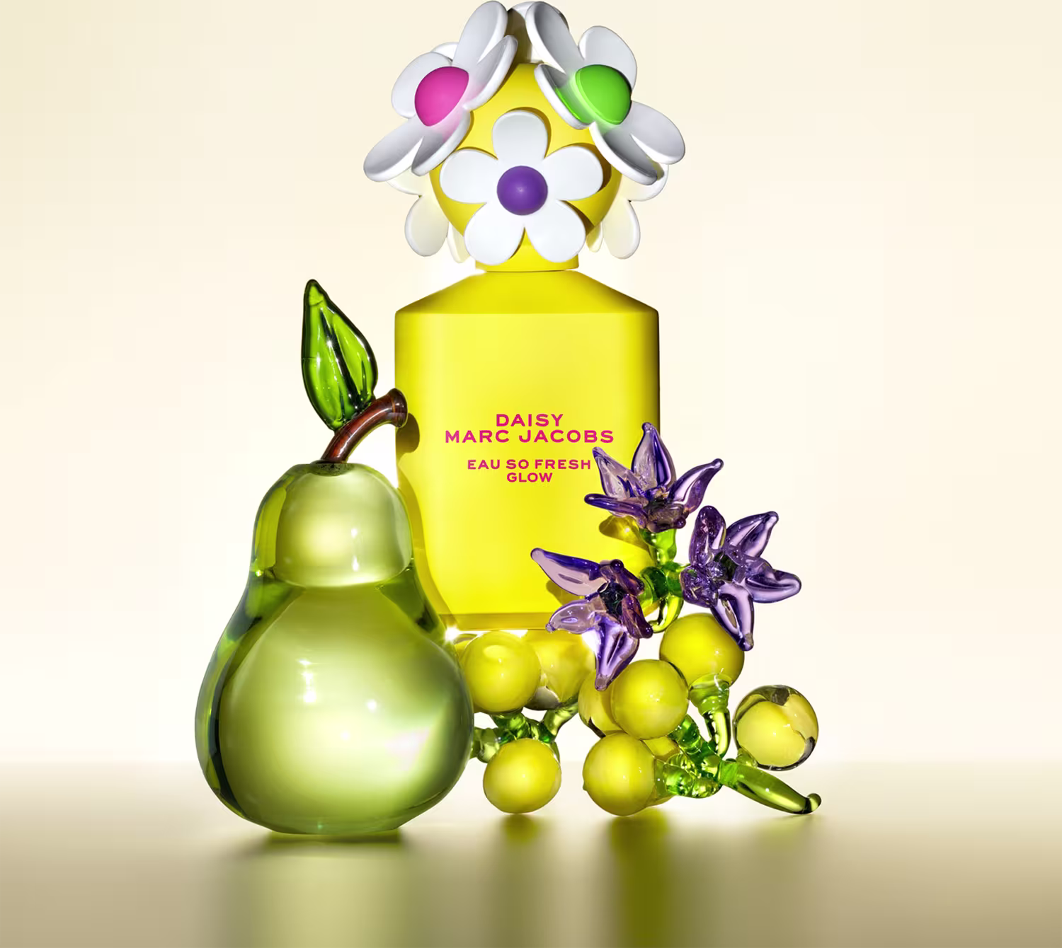 Frasco de perfume Daisy Marc Jacobs Eau So Fresh Glow em embalagem amarela com flores brancas, verdes e roxas decorativas. Pêra verde e outros elementos florais complementam a composição.