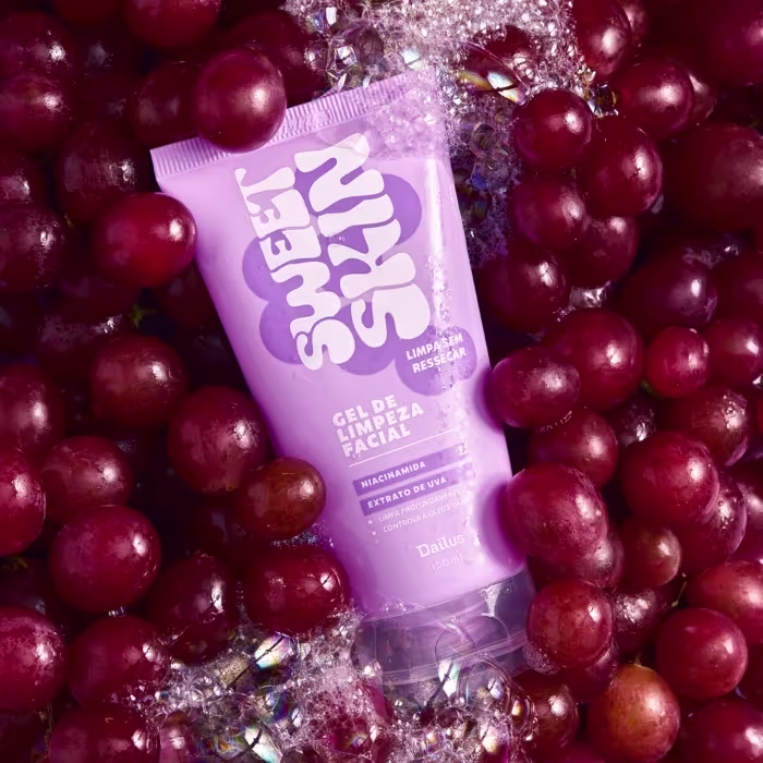 A imagem mostra uma embalagem de 150ml de gel de limpeza facial, tipo bisnaga lilás com letras em branco, em meio a uvas rosadas.