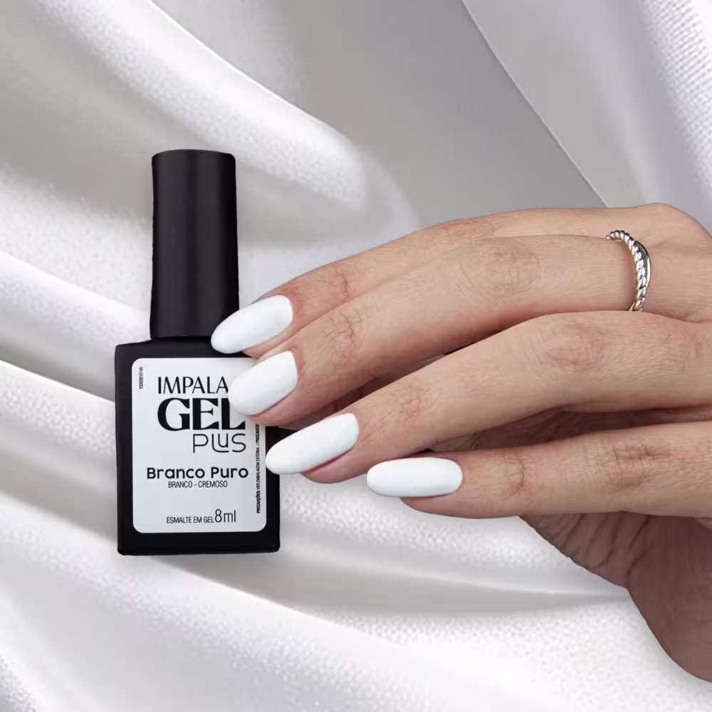 A mão de uma pessoa segura um esmalte em gel da marca Impala em um ambiente claro e minimalista, com tecido branco ao fundo, sugerindo um contexto de aplicação de produtos de beleza.