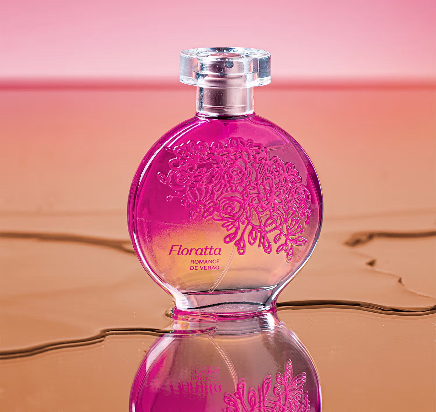 Perfume em frasco de vidro rosa vibrante. O frasco tem formato arredondado com detalhes gravados em relevo floral na parte frontal. A tampa é de plástico transparente. O frasco reflete a luz, criando um efeito brilhante.