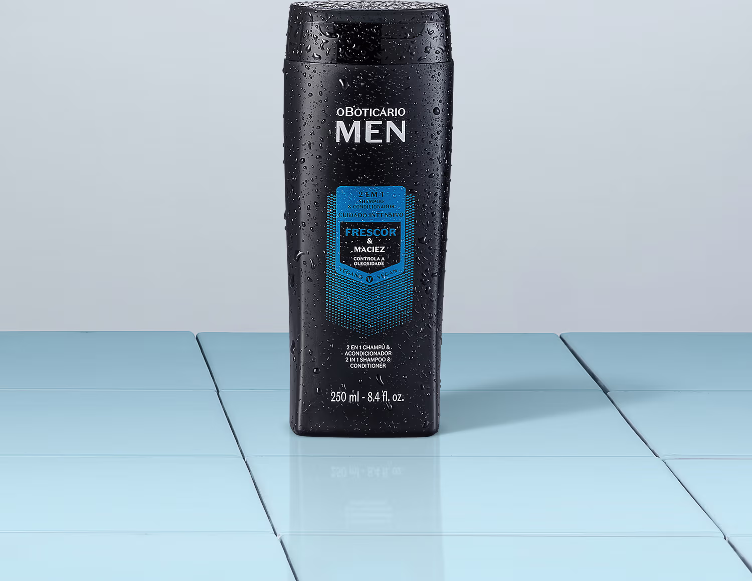 Na imagem um shampoo e condicionador 2 em 1 para cabelos masculinos, da linha o Boticário Men. A embalagem é preta com detalhes em azul e o frasco tem capacidade de 250ml. Está posicionado sobre uma superfície azul clara e reflexiva.