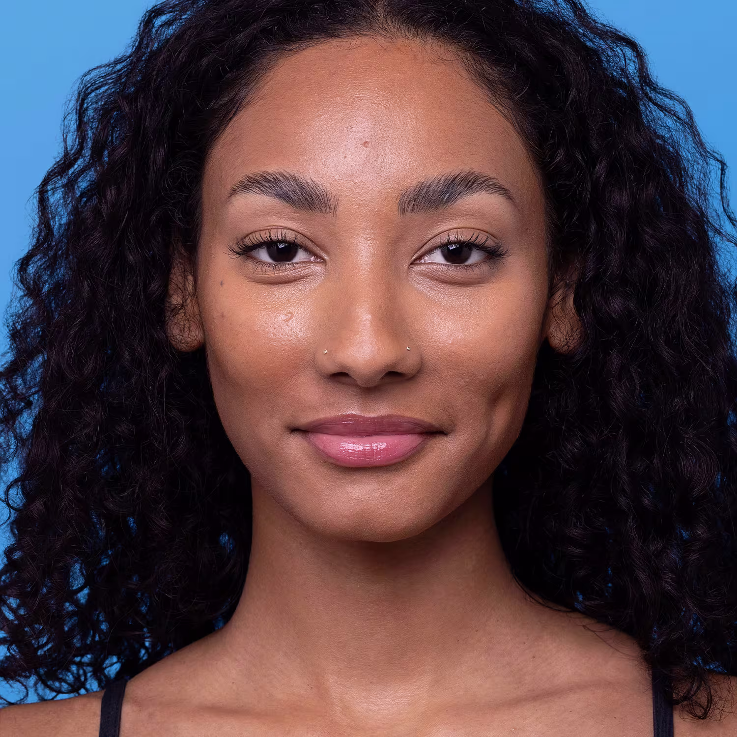 Retrato de uma mulher com cabelos escuros e pele negra em um fundo azul, sugerindo um ambiente de produto de beleza da marca Boti Sun.