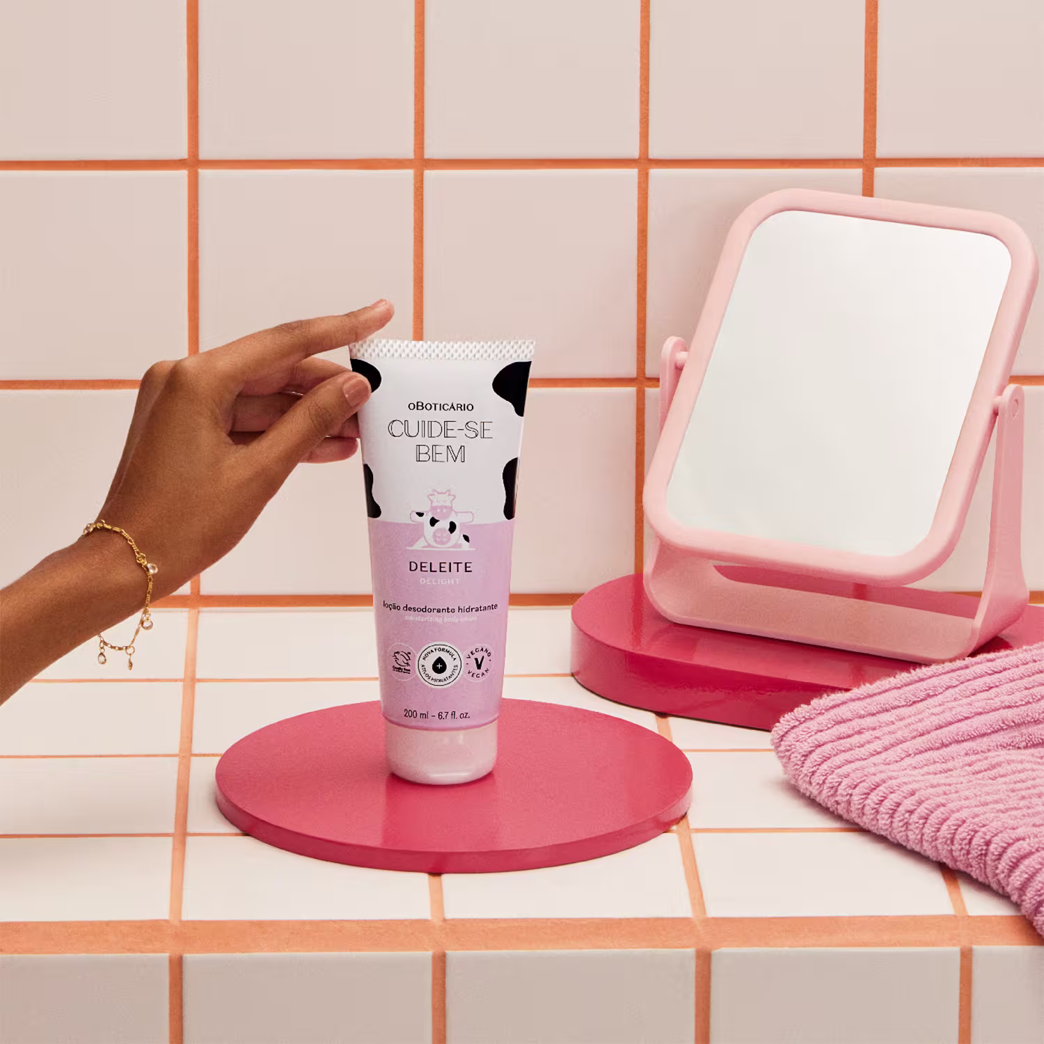 O produto exibido na imagem é um hidratante desodorante da marca Cuide-se bem, com o nome "Deleite". O frasco é branco e rosa, com um design gráfico de uma vaca. O produto está posicionado em uma superfície rosa, junto a um espelho de mesa também rosa.