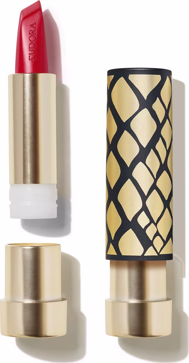Na imagem o Batom Eudora Glam Amulips. O batom está aberto, revelando seu interior com o nome Eudora gravado no produto. A embalagem com design geométrico em preto e dourado, com um padrão de losangos que se entrelaçam, formam uma textura elegante.