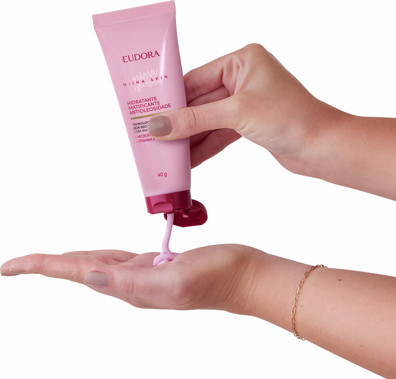 Imagem de mão segurando o tubo de creme hidratante. O tubo é rosa e tem uma consistência cremosa, sendo expelido diretamente na palma da outra mão. A mão que segura o tubo está com uma pulseira delicada, denotando um toque de elegância na imagem.