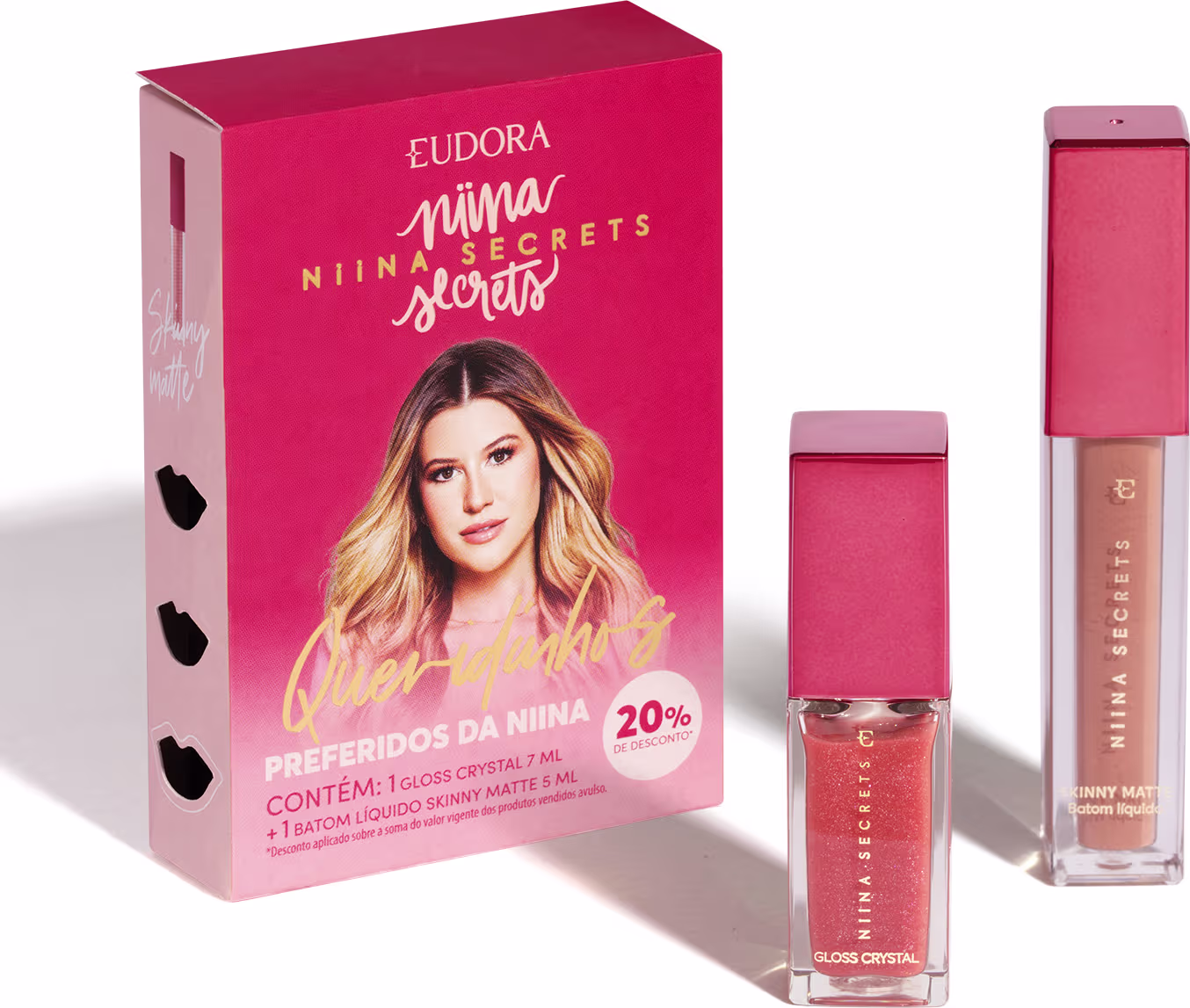 A imagem mostra um kit com um batom e um gloss labial, eles estão lado a lado do lado direito, ambos num frasco quadrado transparente, de tampa rosa, com o nome da linha em dourado. Do lado esquerdo, a caixa do kit, toda rosa com a imagem da dona da linha