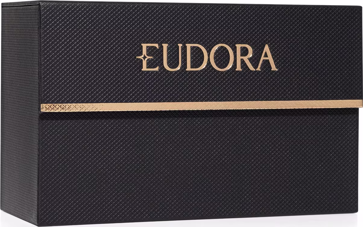 A imagem mostra uma caixa preta, com textura de malha, e possui detalhes dourados com o nome "Eudora" em letras estilizadas, denotando um visual glamuroso e refinado.