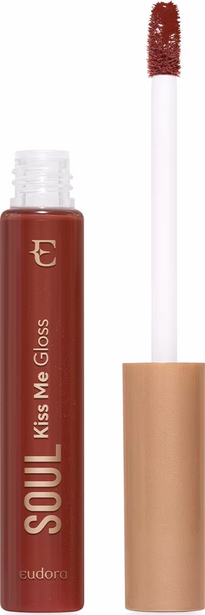 Frasco de vidro transparente contendo gloss marrom caramelo achocolatado. Rótulo com o nome do produto e da marca em letras douradas sobre fundo transparente do frasco e marrom do produto. Aplicador de espuma em formato de pincel firme. Tampa dourada