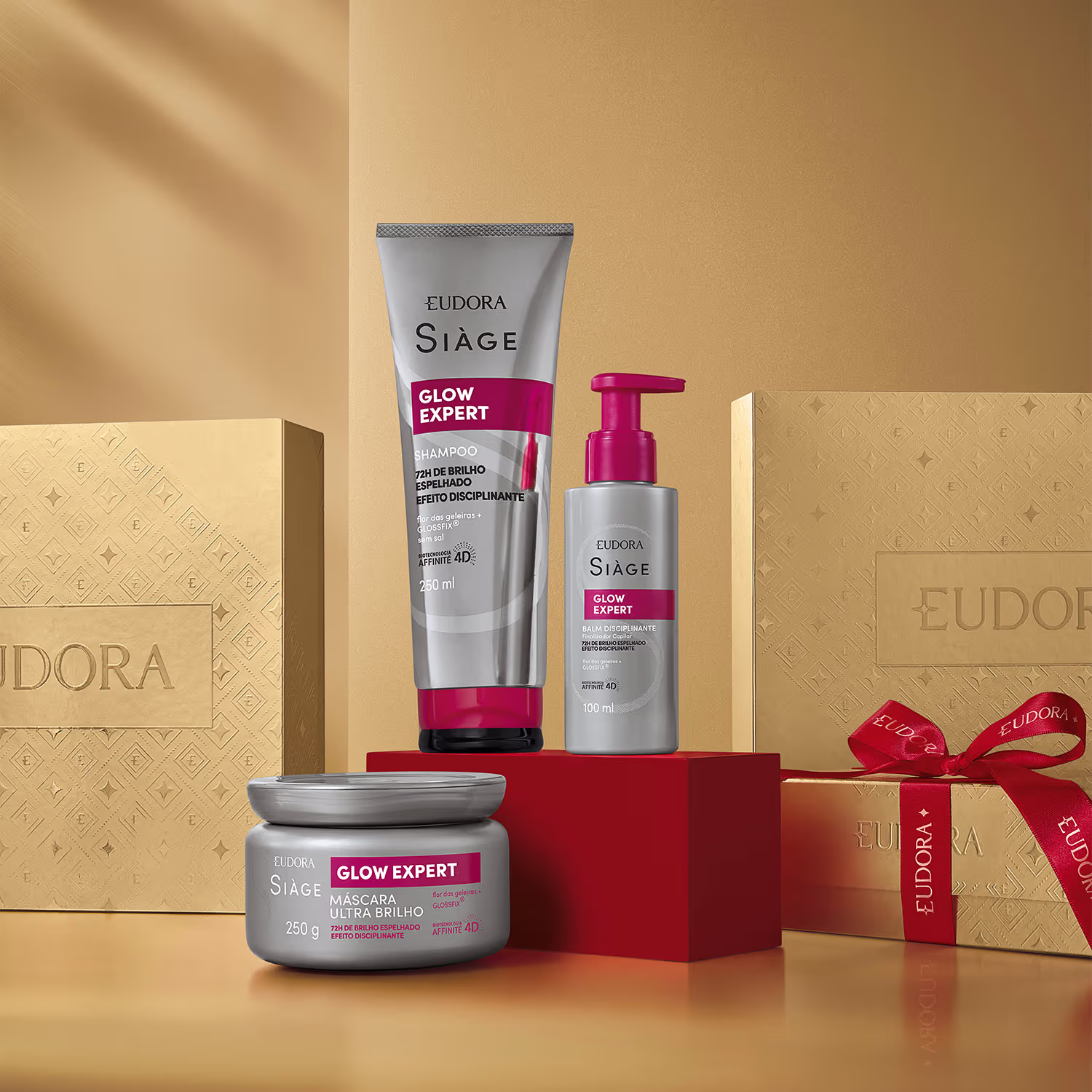 A imagem mostra produtos da linha Glow Expert da marca Siàge sobre uma caixa vermelha. Ao redor caixas douradas com o nome Eudora e  fita vermelha decorativa.