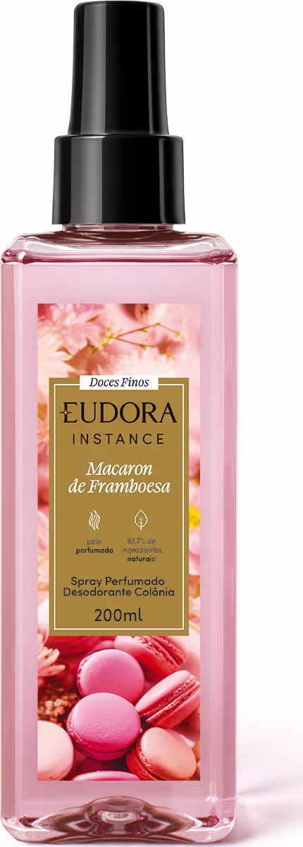 A imagem mostra um frasco transparente retangular, com o body spray de cor rosa claro. No rótulo, desenhos de macarons e flores delicadas, com um retângulo dourado onde estão as informações do produto. A tampa do pulverizador é preta.