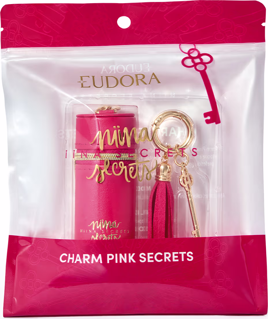 Embalagem rosa com detalhes dourados contendo um acessório da marca Niina Secrets, com pingente e borla decorativa.