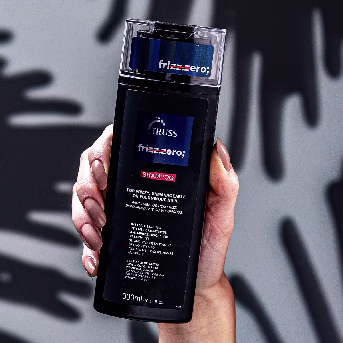 A imagem mostra um shampoo da marca Truss, linha Frizz.zero, voltada para cabelos frizados, indisciplinados ou volumosos. O frasco plástico é preto com detalhes em azul escuro, e apresenta o logotipo da marca "TRUSS frizz.zero;"