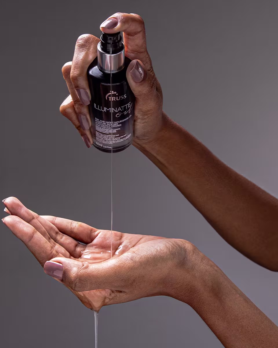 A imagem mostra mãos segurando um frasco escuro de um produto capilar chamado "Illuminatte" da marca Truss. O produto é um óleo destinado a iluminar ou realçar os fios de cabelo.