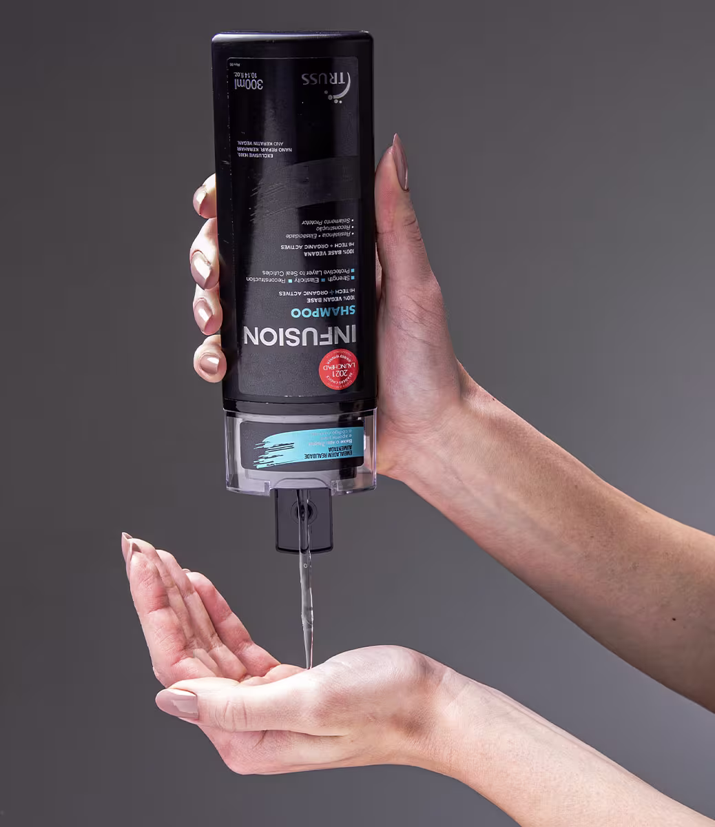 A imagem mostra uma mão segurando um frasco de shampoo da marca Truss, linha Infusion. Também é possível ver o seu conteúdo, que é cremoso e transparente.