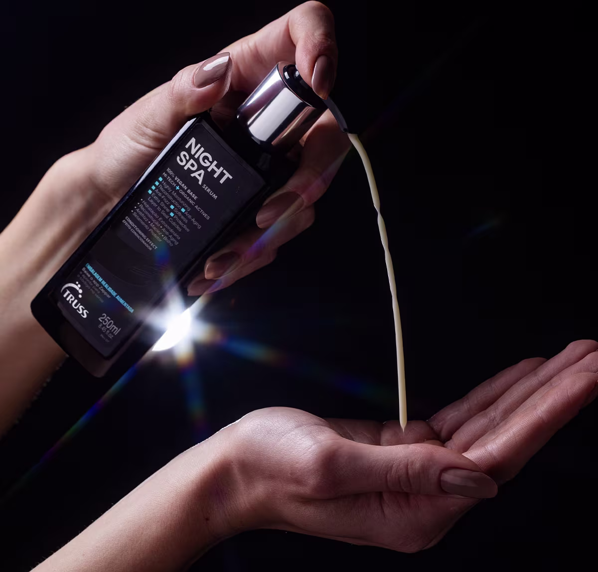 A imagem mostra um frasco de um produto chamado "Night Spa", um sérum capilar. O frasco está sendo segurado por mãos femininas contra um fundo preto. A embalagem tem um design elegante e moderno, com letras destacando o nome do produto.