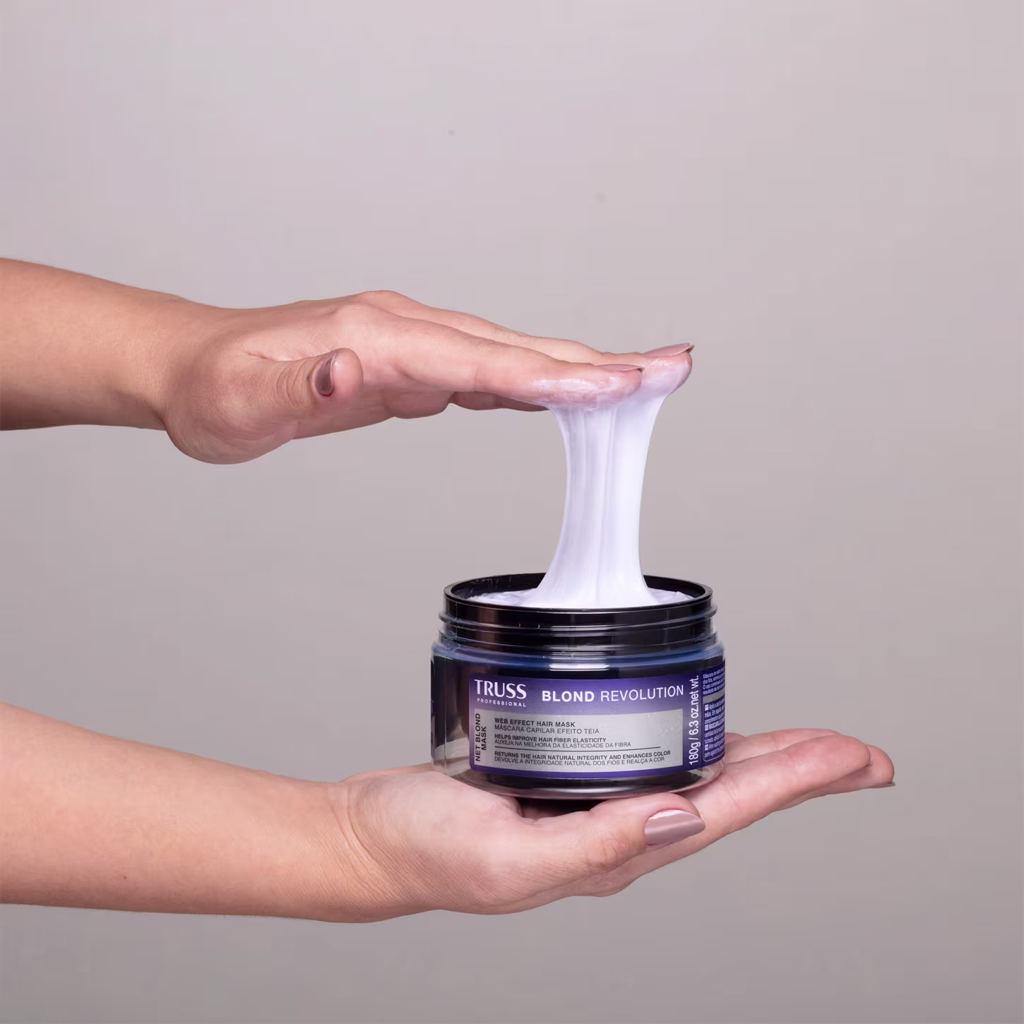 Imagem mostra uma mão segurando o pote da máscara e o outra mão pegando uma amostra do produto, exemplificando o efeito teia.