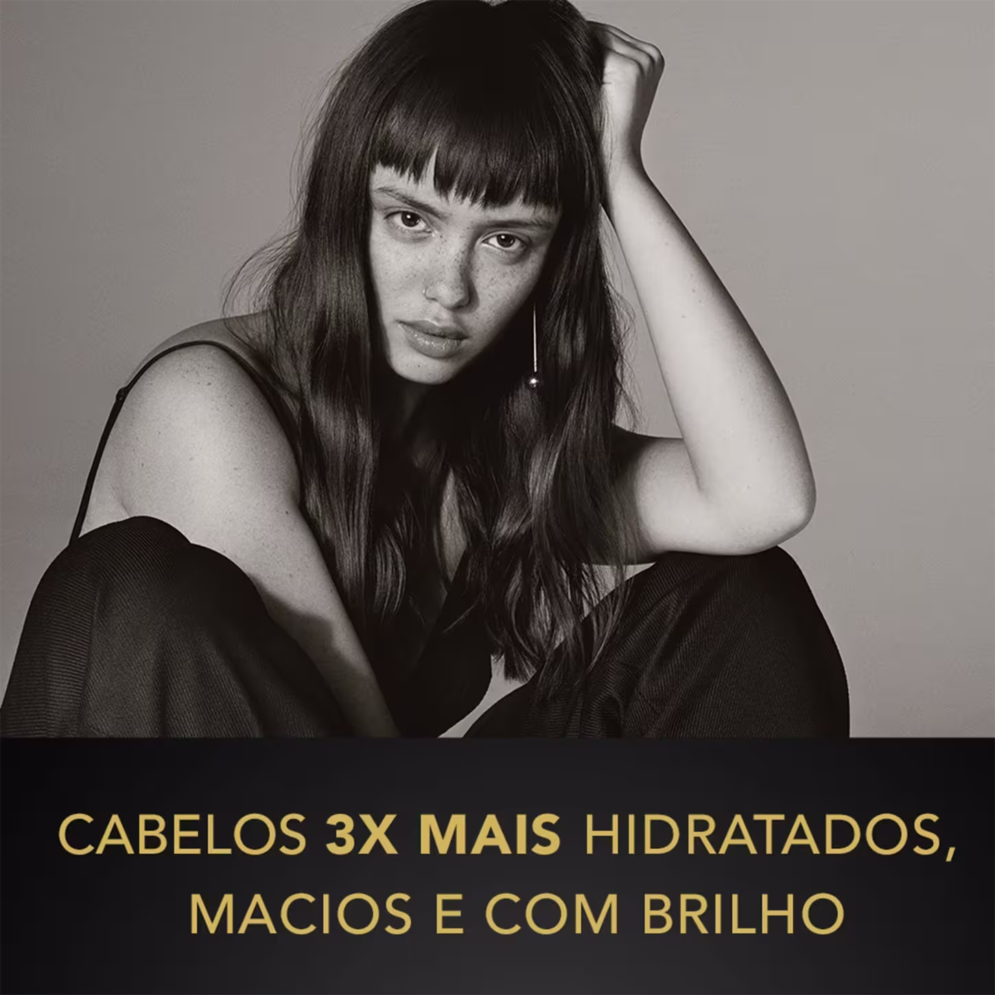 A imagem apresenta uma mulher jovem com longos cabelos escuros e franja, em um close retrato em preto e branco. Ela está usando um top preto transparente e tem uma expressão séria, com uma mão apoiando a cabeça.