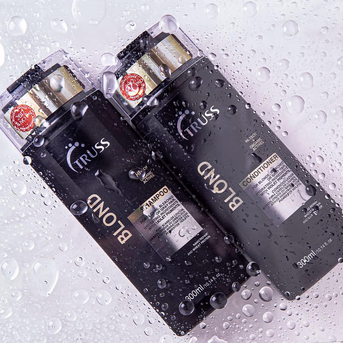 Dois frascos de shampoo e condicionador da marca Truss. Embalagens cilíndricas pretas com detalhes em dourado e prata. Rótulos com o logotipo Truss. Gotas de água condensadas cobrindo as superfícies dos frascos, criando um efeito molhado.