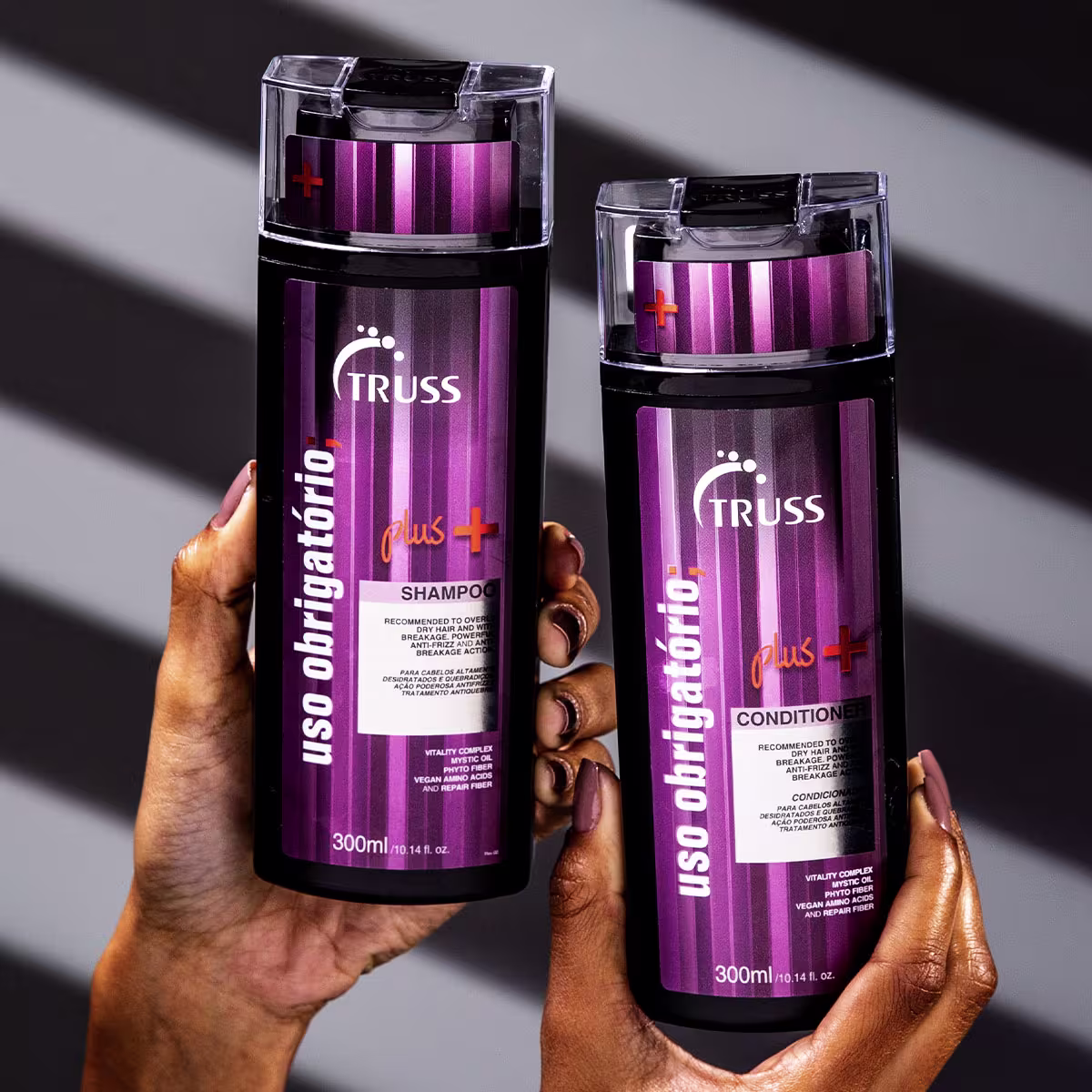 Shampoo e condicionador Truss Plus em frascos cilíndricos transparentes de 300ml. Os frascos têm tampas pretas e rótulos roxos com detalhes em vermelho.