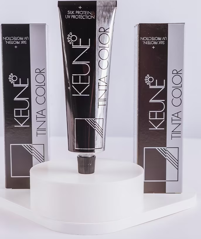 Três caixas de produtos de coloração de cabelo da marca Keune, com embalagens pretas e brancas, exibindo o nome da marca e informações sobre a composição e proteção UV.