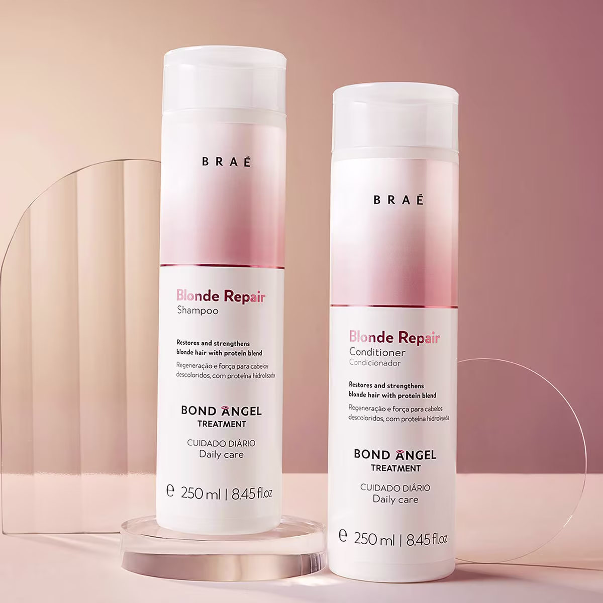 São produtos para cabelos loiros da marca Braé. Há dois frascos de plástico brancos com degradê rosa, um shampoo e um condicionador da linha Blonde Repair, com rótulos indicando que restauram e fortalecem os cabelos loiros com uma mistura de proteínas.