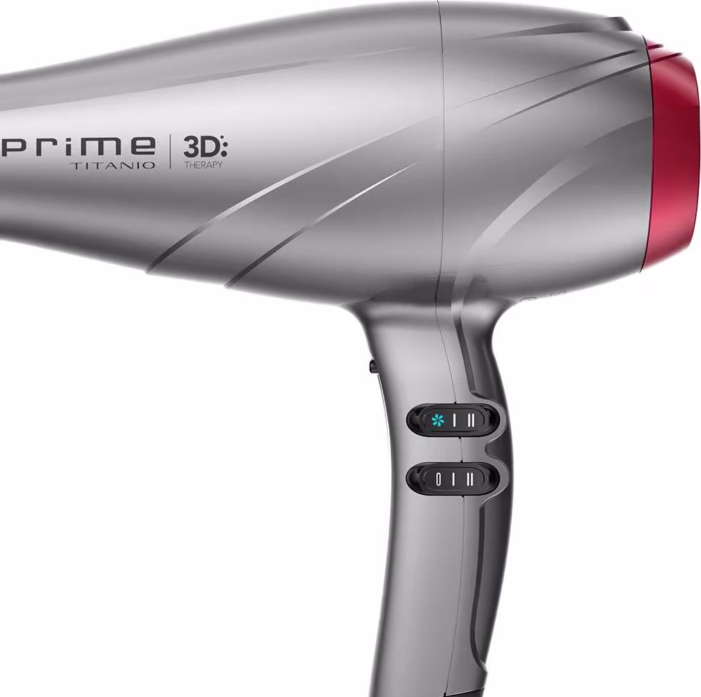 A imagem traz o secador de cabelo da GA.MA Italy Prime 3D Titanio. O acessório possui um corpo alongado e aerodinâmico em plástico cinza e detalhes em vermelho. O cabo traz dois botões par ajustar a temperatura e a velocidade do acessório.