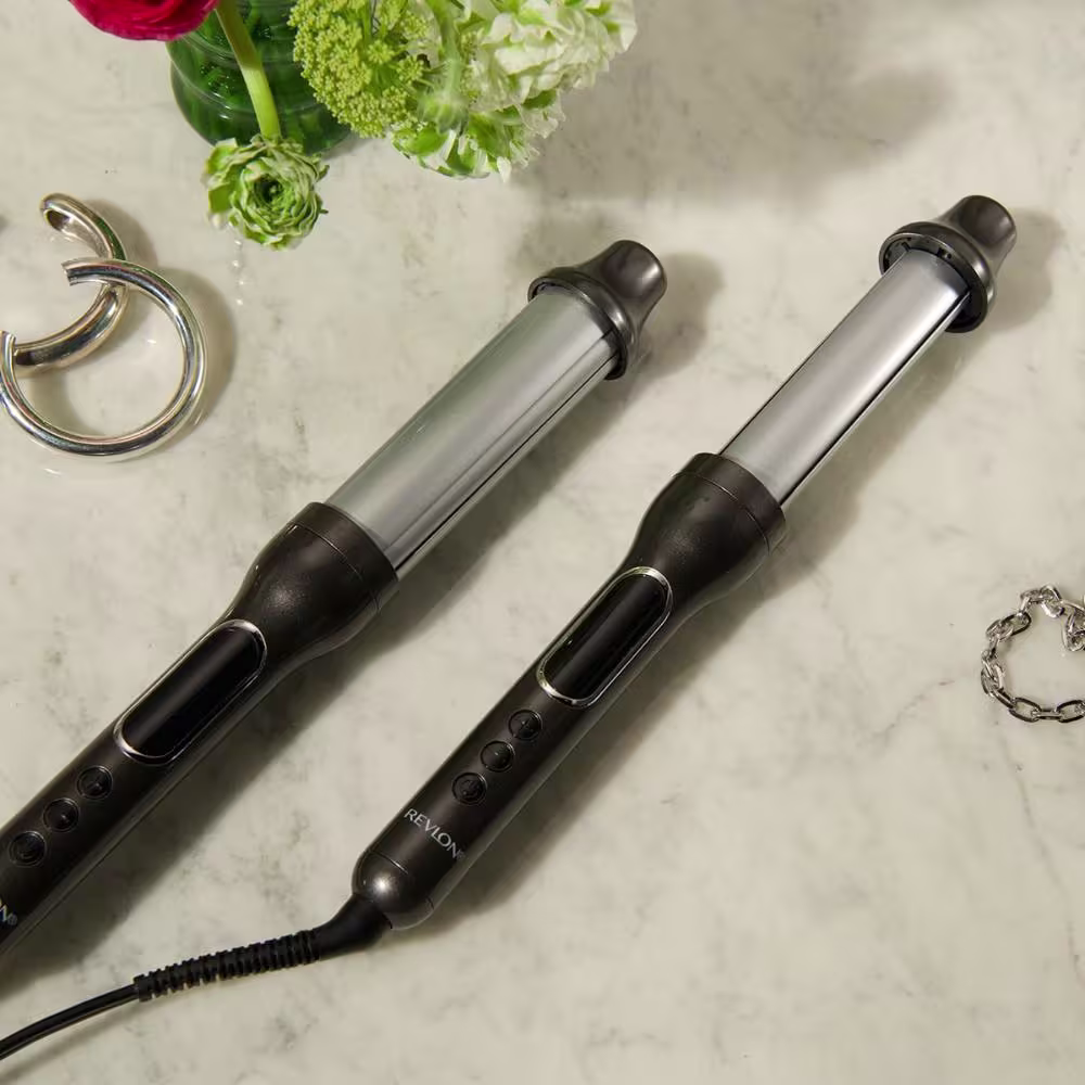 Dois modeladores de cabelo profissionais da marca Revlon. Os modeladores são cilíndricos, em metal escovado e plástico preto. Possuem hastes longas com punhos emborrachados e vários botões de controle.