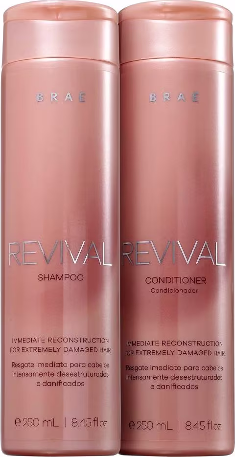 São dois frascos de plástico rígido na cor rosa metálico, contendo shampoo e condicionador da linha Revival da marca Brae. Os frascos têm formato cilíndrico e tampa rosqueável na mesma tonalidade.