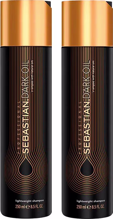 A imagem mostra dois Shampoos Dark Oil da marca Sebastian Professional. Os frascos são cilíndricos e escuros, com detalhes em dourado. Apresentam o logotipo e nome da marca "Sebastian Dark Oil" em letras douradas estilizadas.