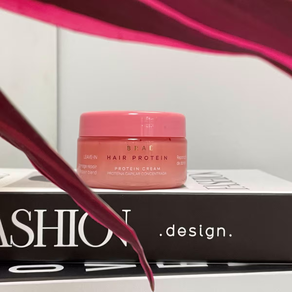 Produto de tratamento capilar Braé Hair Protein. Embalagem em pote plástico arredondado na cor coral.  Produto posicionado sobre uma caixa preta.
